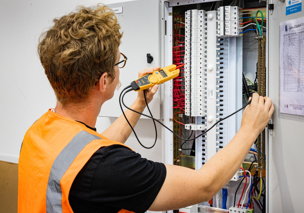 Applied Electrical team member working on a switchboard in hi-vis vest